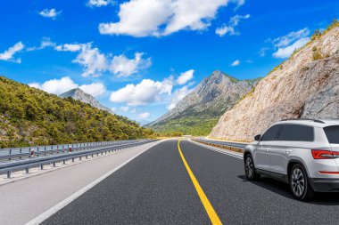 Güneşli bir günde, beyaz bir araba kayalık dağların arka planına doğru yol alır..