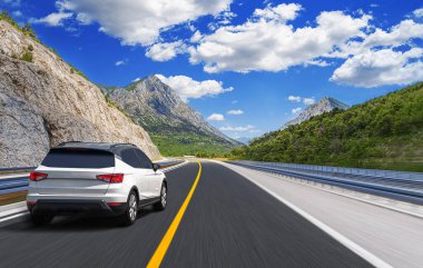 Güneşli bir günde, beyaz bir araba kayalık dağların arka planına doğru yol alır..