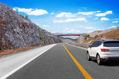 Beyaz araba otobanda sürüyor, arkasında dağlar var. Araba yolculuğu - kavram.