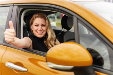 Kendine güvenen sarışın bir kadın sarı bir arabada oturuyor, gülümsüyor ve pencereden baş parmak işareti yapıyor, başarıyı, mutluluğu ve bağımsızlığı simgeliyor..