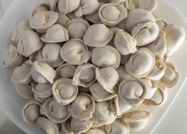 Çiğ, donmuş pelmeni dolu bir tabak, etle doldurulmuş geleneksel hamur köfteleri, farklı şekillerini ve dokularını gösteriyor..