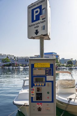 Zadar, Hırvatistan - 29 Temmuz 2021: Hırvatistan 'ın Zadar kentinde bir marinaya yakın park metresi, arka planda manzaralı bir liman manzarası bulunan SMS ve kredi kartı da dahil olmak üzere birden fazla ödeme seçeneği sunuyor.