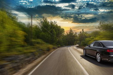 Pürüzsüz, siyah bir araba, hareketli bir günbatımında dolambaçlı bir orman yolunda hızla ilerliyor. Seyahatin heyecanını ve hareketli doğanın güzelliğini yakalıyor..