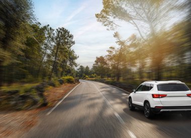 Beyaz bir SUV hızla güneşli bir orman yolunda ilerliyor. Özgürlüğün, hızın ve açık hava macerasının ruhunu yakalıyor..