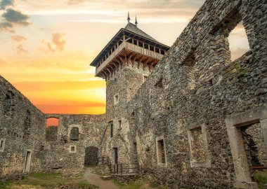 Nevytsky Şatosu, Ukrayna 'nın Uzhhorod yakınlarındaki yeşil bir yamaçta parlayan bir günbatımı gökyüzüne karşı duran ortaçağ kalıntısı..