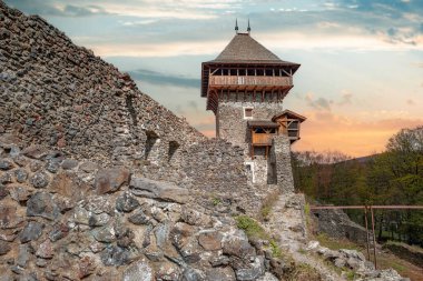 Nevytsky Şatosu, Ukrayna 'nın Uzhhorod yakınlarındaki yeşil bir yamaçta parlayan bir günbatımı gökyüzüne karşı duran ortaçağ kalıntısı..