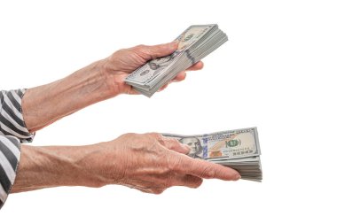 Yaşlı bir insanın elleri, beyaz bir arka planda yapılan mali işlemleri ya da para alışverişini sembolize eden, kalın bir yığın 100 dolarlık banknotu transfer ederken görülüyor..