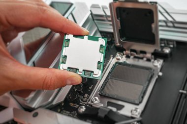 Bir kişi, bir bilgisayar işlemcisini ana kart soketinin üzerinde dikkatlice tutuyor ve yerleştirmeye hazırlanıyor..