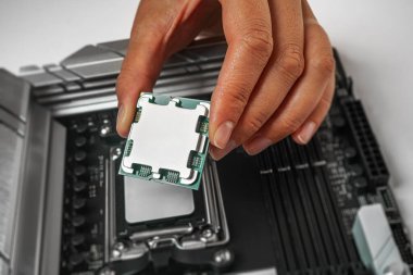 Bir kişi, bir bilgisayar işlemcisini ana kart soketinin üzerinde dikkatlice tutuyor ve yerleştirmeye hazırlanıyor..