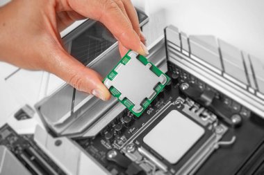 Bir kişi, bir bilgisayar işlemcisini ana kart soketinin üzerinde dikkatlice tutuyor ve yerleştirmeye hazırlanıyor..