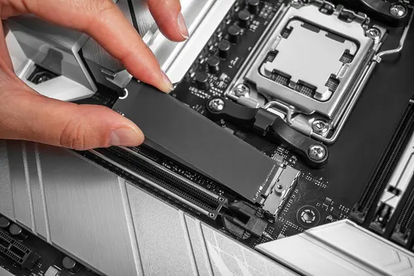 Bir kişi modern bir ana kart soketine bir M2 NVME SSD yüklüyor, bilgisayar donanımı montajı devam ediyor.