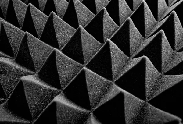 Siyah akustik köpük paneller, ses emmek ve stüdyo ortamlarında yankıyı azaltmak için tasarlanmış keskin, geometrik bir desen şeklinde düzenlenmiştir..