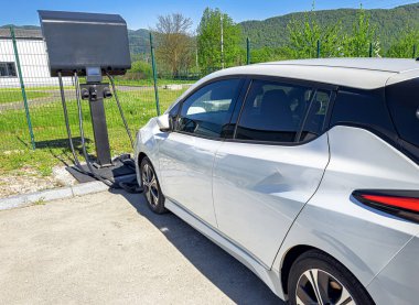 Bir elektrikli araç park edilmiş ve yeşil çevresi olan manzaralı bir açık hava istasyonuna bağlanmış durumda..