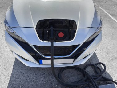 Bir elektrik aracı, ön montajlı şarj limanı ve ağır güç kablosu üzerinden bir istasyonda şarj ediliyor..