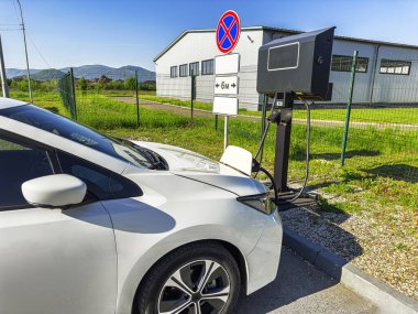 Bir elektrikli araç park edilmiş ve yeşil çevresi olan manzaralı bir açık hava istasyonuna bağlanmış durumda..