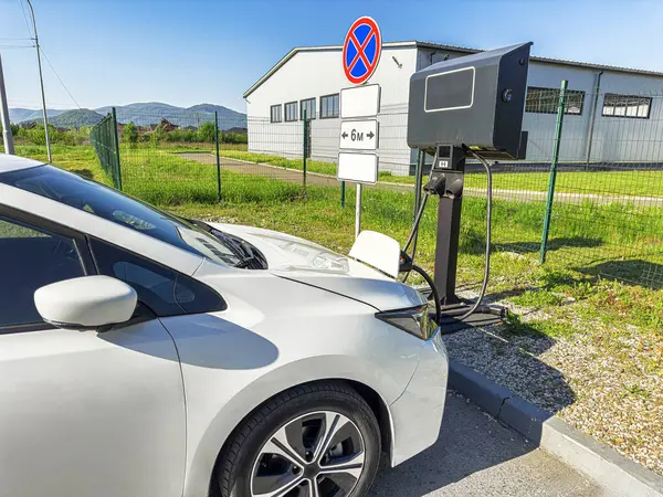 Bir elektrikli araç park edilmiş ve yeşil çevresi olan manzaralı bir açık hava istasyonuna bağlanmış durumda..