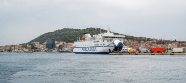 Split, Hırvatistan - 25 Temmuz 2023: Hırvatistan 'ın Split limanına yanaşan büyük feribot, çevresindeki kargo kamyonları ve kıyı tepeleri ve şehir binaları manzaralı bir zemin hazırladı.