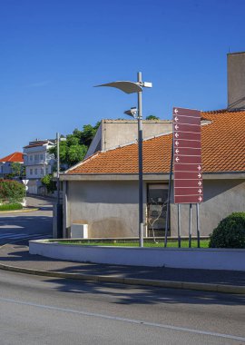 Modern sokak lambasıyla sokak manzarası, çoklu oklu bir yön işareti ve açık mavi gökyüzünün altında kırmızı kiremitli çatıları olan binalar..