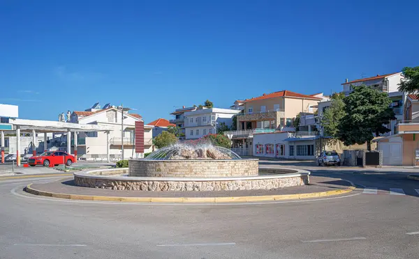 Primosten 'de açık mavi bir gökyüzünün altında, Akdeniz tarzı evlerle çevrili sakin bir kavşağın ortasına su püskürten dairesel taş çeşme..