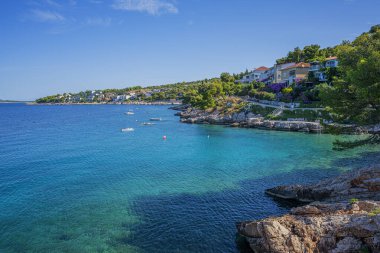 Berrak mavi suları, çam ağaçları, kayalık kıyıları ve güneşli bir gökyüzünün altındaki uzak adaları olan sakin bir Akdeniz sahili..