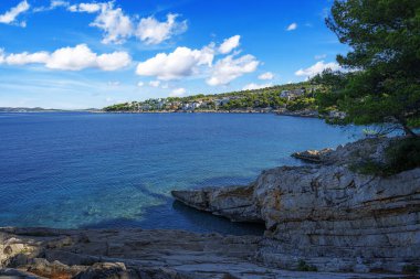 Berrak mavi suları, çam ağaçları, kayalık kıyıları ve güneşli bir gökyüzünün altındaki uzak adaları olan sakin bir Akdeniz sahili..