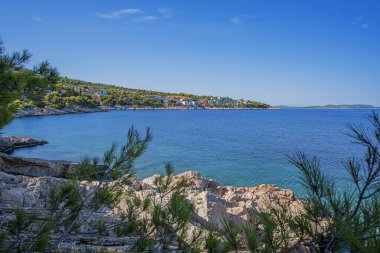 Berrak mavi suları, çam ağaçları, kayalık kıyıları ve güneşli bir gökyüzünün altındaki uzak adaları olan sakin bir Akdeniz sahili..