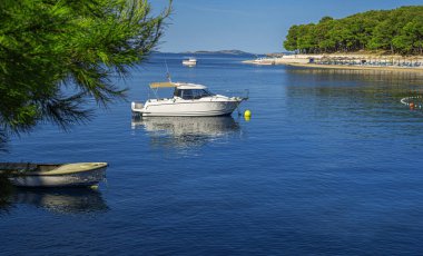 Birkaç küçük tekne sakin, berrak mavi deniz sularında yüzüyor. Parlak mavi gökyüzünün altında uzak bir sahil köyü var..