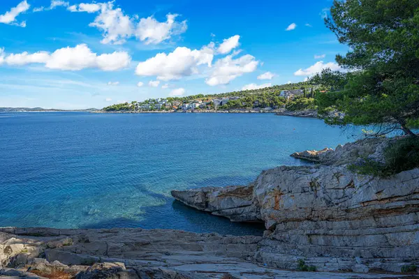 Berrak mavi suları, çam ağaçları, kayalık kıyıları ve güneşli bir gökyüzünün altındaki uzak adaları olan sakin bir Akdeniz sahili..