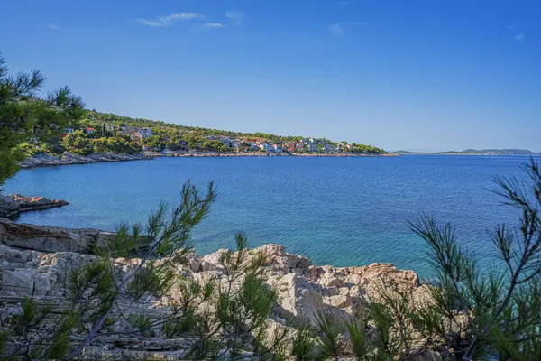 Berrak mavi suları, çam ağaçları, kayalık kıyıları ve güneşli bir gökyüzünün altındaki uzak adaları olan sakin bir Akdeniz sahili..