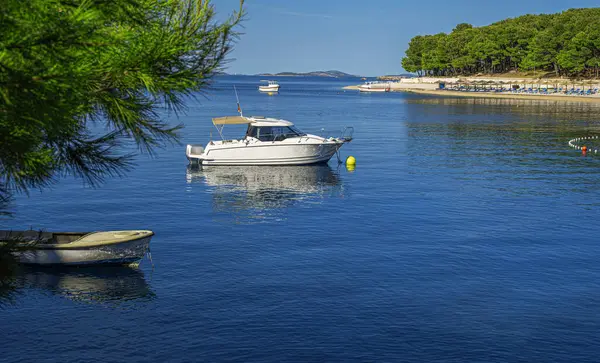 Birkaç küçük tekne sakin, berrak mavi deniz sularında yüzüyor. Parlak mavi gökyüzünün altında uzak bir sahil köyü var..