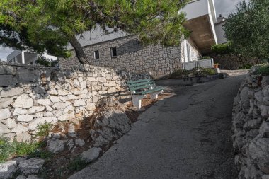 Sakin bir sahil yolunda, parlak mavi bir gökyüzünün altında tüylü bulutlarla, sakin bir Akdeniz köyü atmosferini anımsatan geleneksel taş ev..