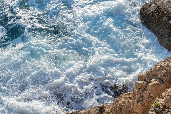 Okyanus dalgaları güçlü ve dinamik bir köpüklü beyaz su ve doğal kuvvet gösterisi oluşturan kayalık bir uçuruma enerjiyle çarpar..