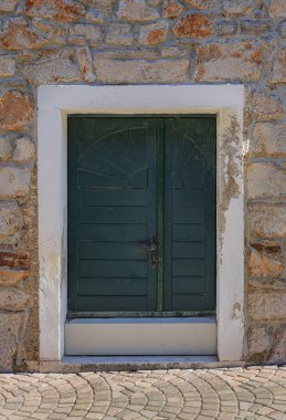 Taştan bir duvarda beyaz bir çerçeve ve süslemeli ahşap bir kapı, tarihi ve büyüleyici bir mimari tarzı çağrıştırıyor..
