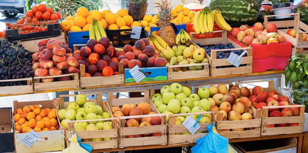 Canlı bir açık hava tezgahı, ahşap kasalarda renkli taze meyve çeşitleri sergiliyor. Mevsimlik ödüller sunuyor..