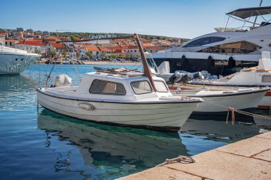 Parlak mavi bir gökyüzünün altında kıyı binaları ve diğer teknelerle berrak, berrak bir marinaya parlak bir motorlu tekne yanaştı..