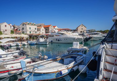 Birçok lüks yat ve tekne, sakin deniz ve uzak yeşil kıyı şeridi ile çevrili güneşli bir marinada demirlemiştir.