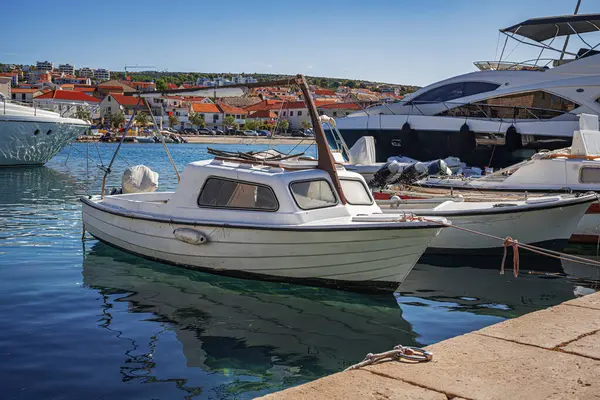 Parlak mavi bir gökyüzünün altında kıyı binaları ve diğer teknelerle berrak, berrak bir marinaya parlak bir motorlu tekne yanaştı..