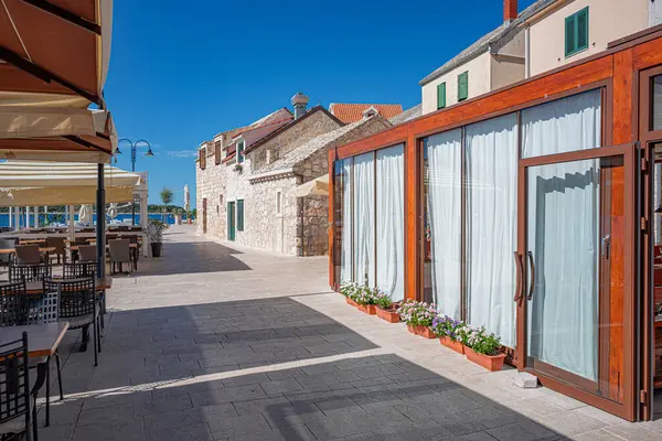 Huzurlu deniz kenarı restoranı, modern ahşap masalar ve büyük şemsiyelerin altında deniz manzaralı bir gezinti alanı boyunca sıralanmış sandalyeler..