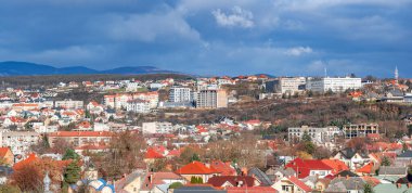Panoramik manzara, Ukrayna 'nın Ukrayna' nın Uzhhorod kentinin renkli çatıları yamaçlardan aşağı dökülüyor, dramatik bulutlu bir gökyüzüne ve uzak dağlara karşı kuruluyor.
