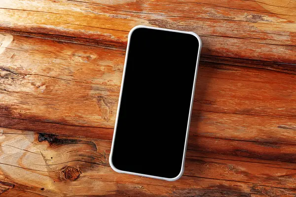 Boş siyah ekranlı modern bir akıllı telefon kırsal ahşap bir yüzey üzerinde çaprazlama uzanır ve temiz ve minimalist bir teknoloji sunumu sağlar..