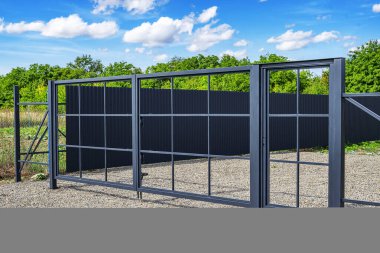 Şebeke dizaynlı modern bir metal kapı çakıllı bir evin önünde, parlak mavi bir gökyüzünün altında duruyor..