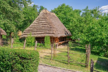 Geniş sazdan çatılı geleneksel ahşap bir ev. Etrafı yemyeşil ağaçlarla çevrili. Huzurlu kırsal bir köyde ahşap bir çit..