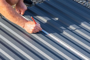 Bir adam titizlikle yuvarlak metal bir levhayı mezura ve kalemle ölçüyor. Çatı ve inşaat işleri için hazırlanıyor..