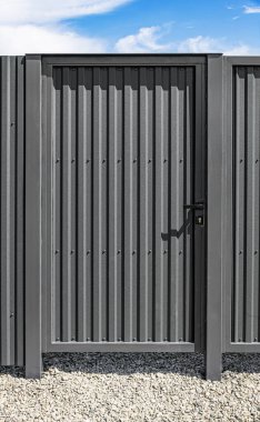 Çelik bir mahremiyet çitine kurulmuş, siyah saplı, modern gri bir metal kapıya yakın plan..