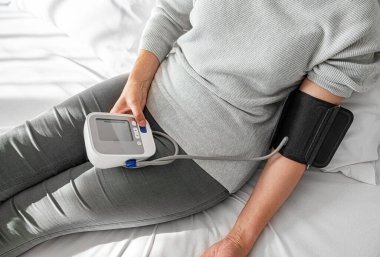 Bir kişi evde otururken dijital monitörle kan basıncını ölçer ve kişisel sağlık ve tıbbi bakım konularına odaklanır..