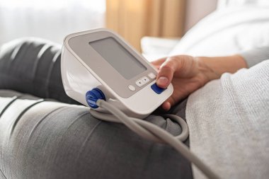 Bir kişi evde otururken dijital monitörle kan basıncını ölçer ve kişisel sağlık ve tıbbi bakım konularına odaklanır..