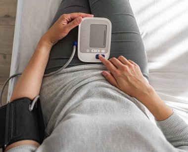 Bir kişi evde otururken dijital monitörle kan basıncını ölçer ve kişisel sağlık ve tıbbi bakım konularına odaklanır..