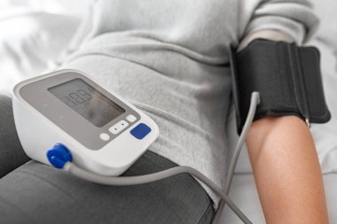 Bir kişi evde otururken dijital monitörle kan basıncını ölçer ve kişisel sağlık ve tıbbi bakım konularına odaklanır..