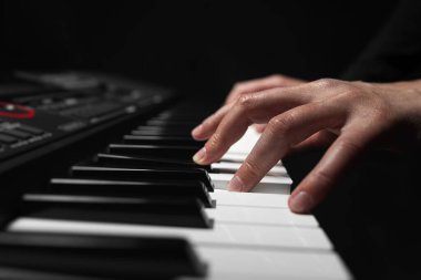 Uzun ince parmaklı bir çift el, yumuşak dramatik bir ışıkla aydınlanan dijital piyanonun beyaz tuşlarına yavaşça bastırır..