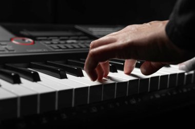 Uzun ince parmaklı bir çift el, yumuşak dramatik bir ışıkla aydınlanan dijital piyanonun beyaz tuşlarına yavaşça bastırır..